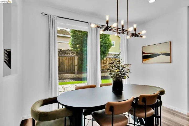 Spacious dining area featuring a modern linear chandelier, wood-finish flooring, and a large window overlooking the backyard with a stone patio