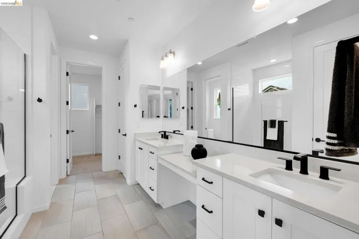 Bright bathroom featuring dual vanities with white cabinetry and countertops, matte black plumbing fixtures, and a frameless mirror