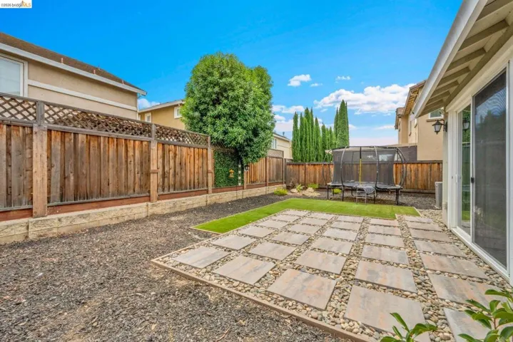 Rear yard featuring a paved patio with stone tile accents, artificial turf, and dark gravel landscaping