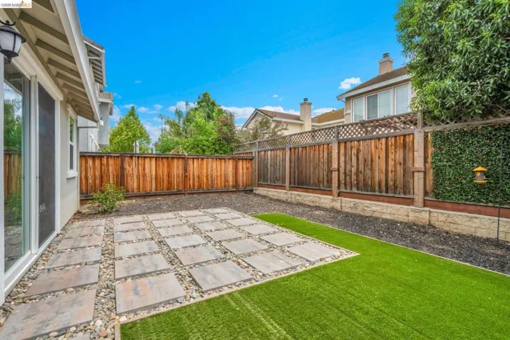Private backyard featuring a stone paver patio, artificial turf, and a wood privacy fence