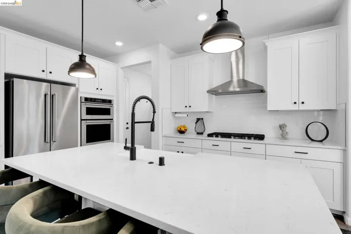 Spacious kitchen featuring an expansive island with a matte black high-arc faucet, white shaker cabinetry, stainless steel appliances, a subway tile backsplash, and recessed lighting