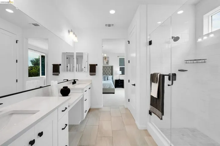 Spacious bathroom featuring a dual vanity with white cabinetry and countertops, a large walk-in shower with subway tile, wood-finish flooring, and recessed lighting