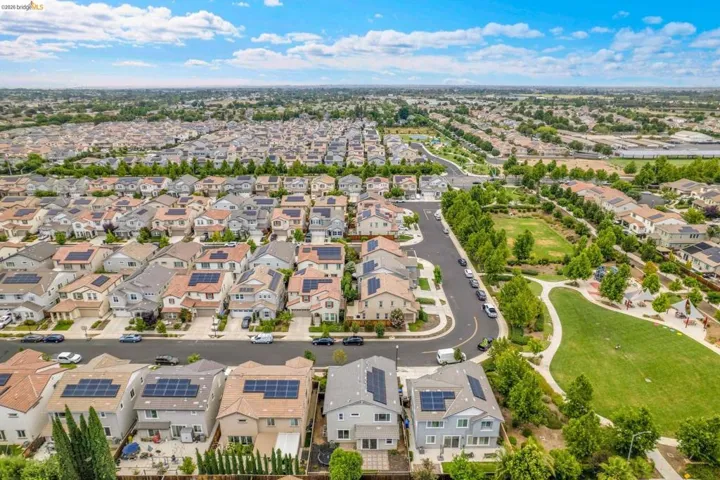 Aerial perspective of a residential neighborhood featuring numerous homes with solar panel installations, community green spaces, paved walking paths, and mature trees
