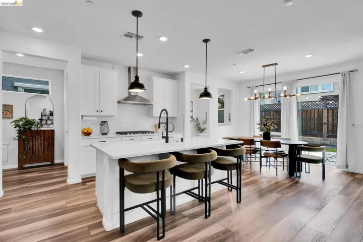 Open-concept kitchen and dining area featuring wood-finish flooring, white cabinetry, a kitchen island with seating, pendant lighting, and a sliding glass door to the exterior