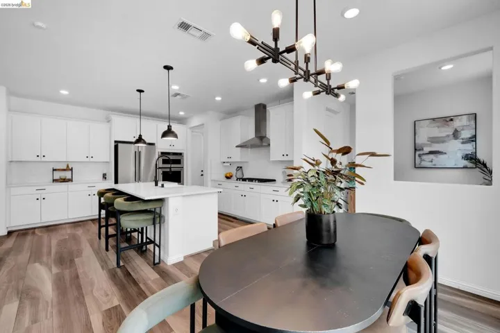 Contemporary kitchen featuring wood-finish flooring, white cabinetry, a large kitchen island with pendant lighting, integrated stainless steel appliances, and a modern dining light fixture