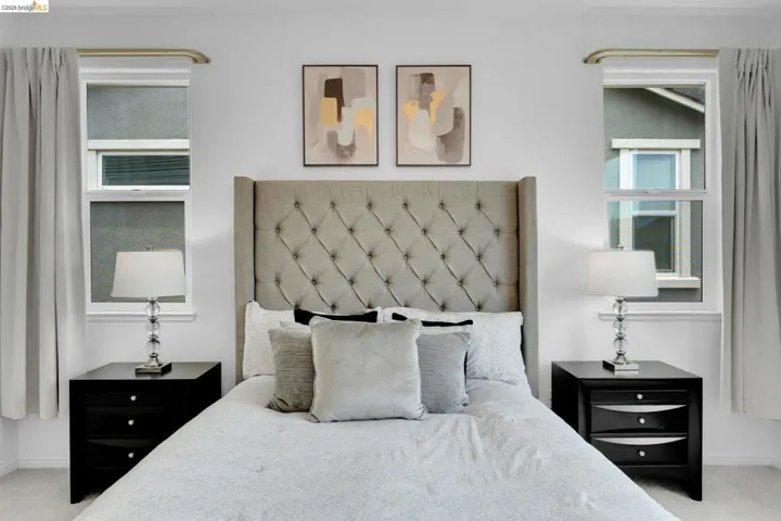 Bedroom featuring a tufted upholstered headboard, dual windows with curtain rods, and two matching nightstands with drawers