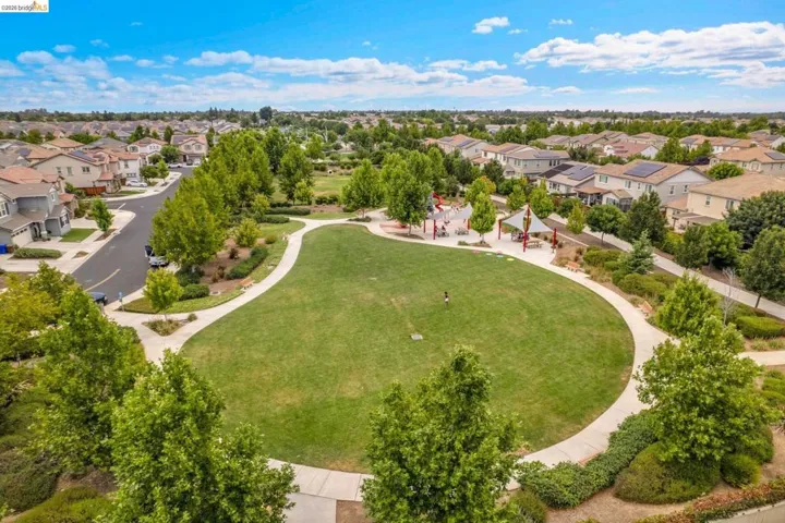 Expansive community green space featuring a manicured lawn, paved walking paths, a dedicated playground area, and mature landscaping