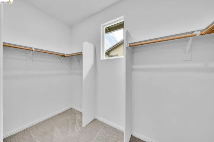 Walk-in closet featuring light beige carpet, white baseboards, and a window