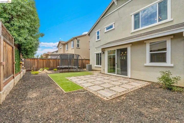 Rear exterior featuring a sliding glass door, a stone-tiled patio, and a section of artificial turf
