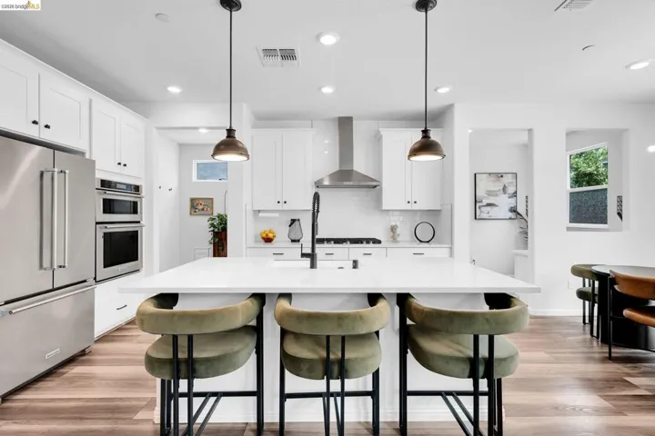 Modern kitchen featuring a large central island with a solid surface countertop, white shaker cabinetry, stainless steel appliances, and wood-finish flooring