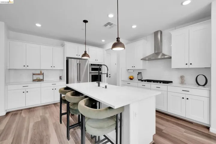 Modern kitchen featuring a large central island, white shaker cabinetry with dark hardware, stainless steel appliances, a subway tile backsplash, and wood-finish flooring