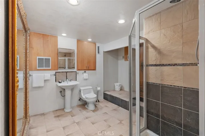 Guest quarters bathroom has storage armoire to right, shower stall and cabinets.