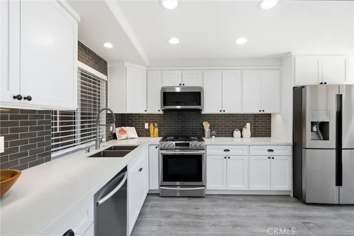 Beautifully appointed kitchen featuring white shaker cabinetry, subway tile backlash, and  stainless steel appliances