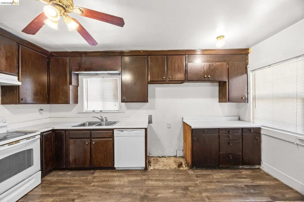 Kitchen featuring wood-finish flooring, dark wood cabinetry, white countertops, and a white dishwasher