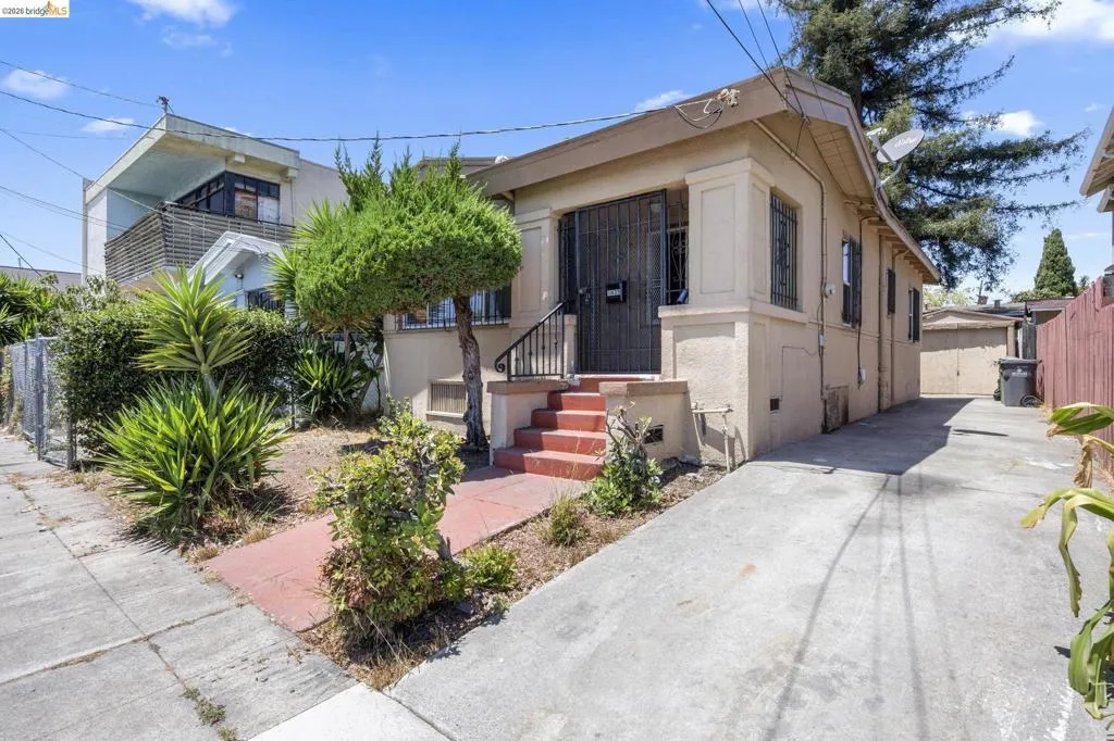 Single-story residence featuring a stucco exterior, concrete driveway, front porch with red-painted steps, and decorative security bars on the front door and windows
