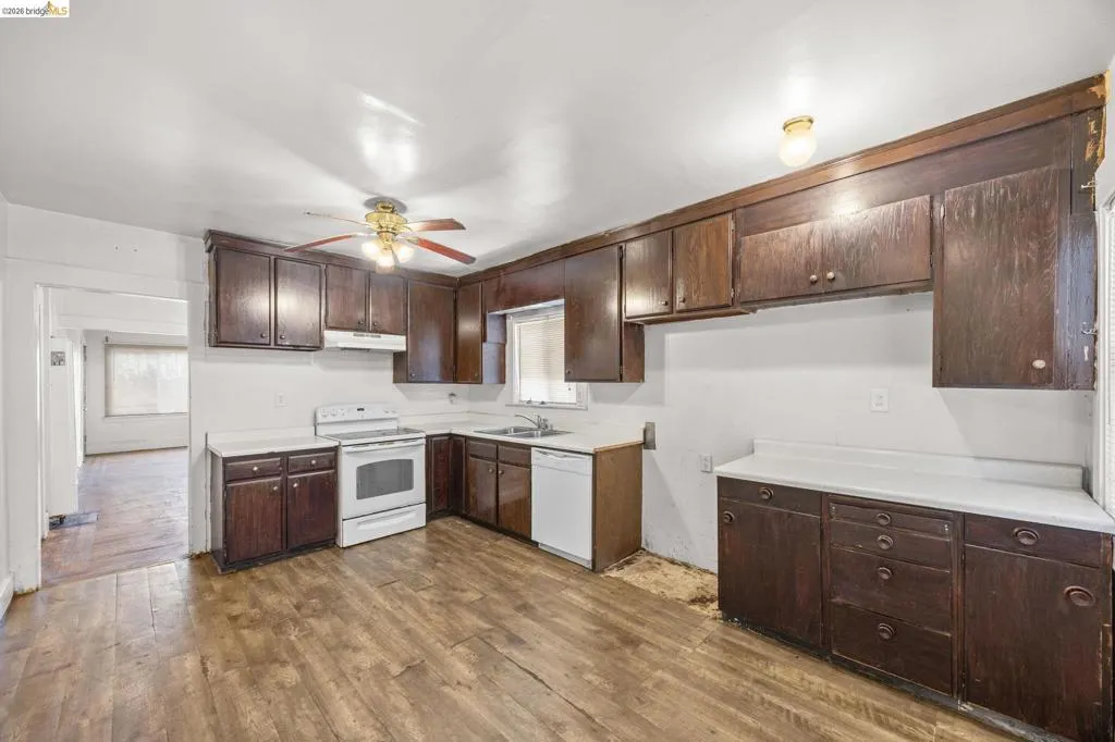 Kitchen featuring extensive dark wood cabinetry, white countertops, white range, white dishwasher, and wood-finish flooring