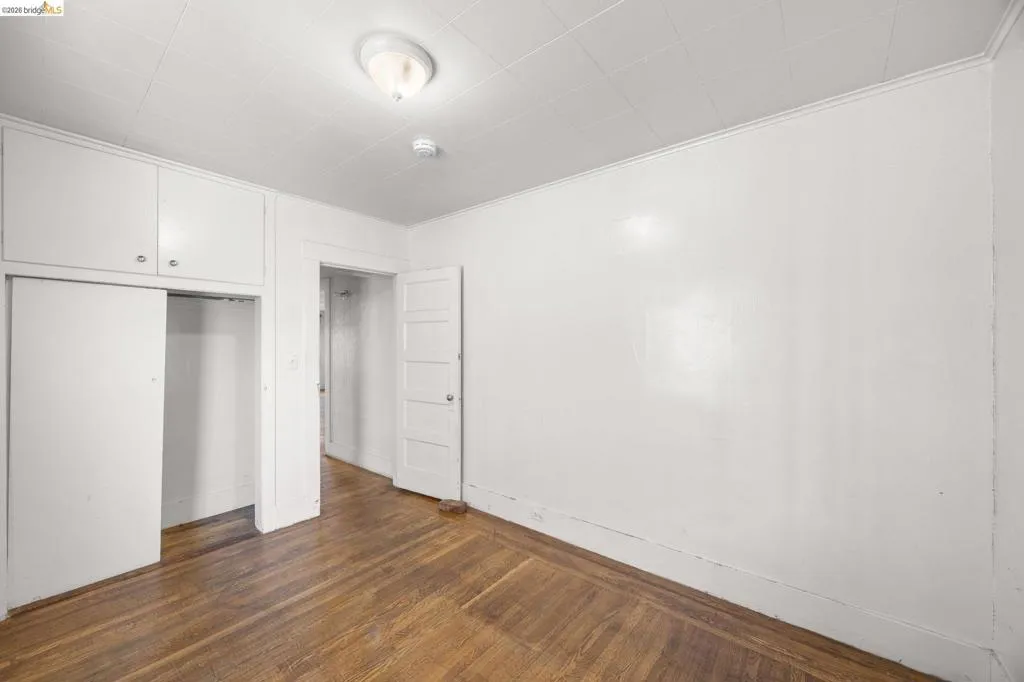Hardwood flooring with natural finish, white walls, and built-in closet with upper cabinetry