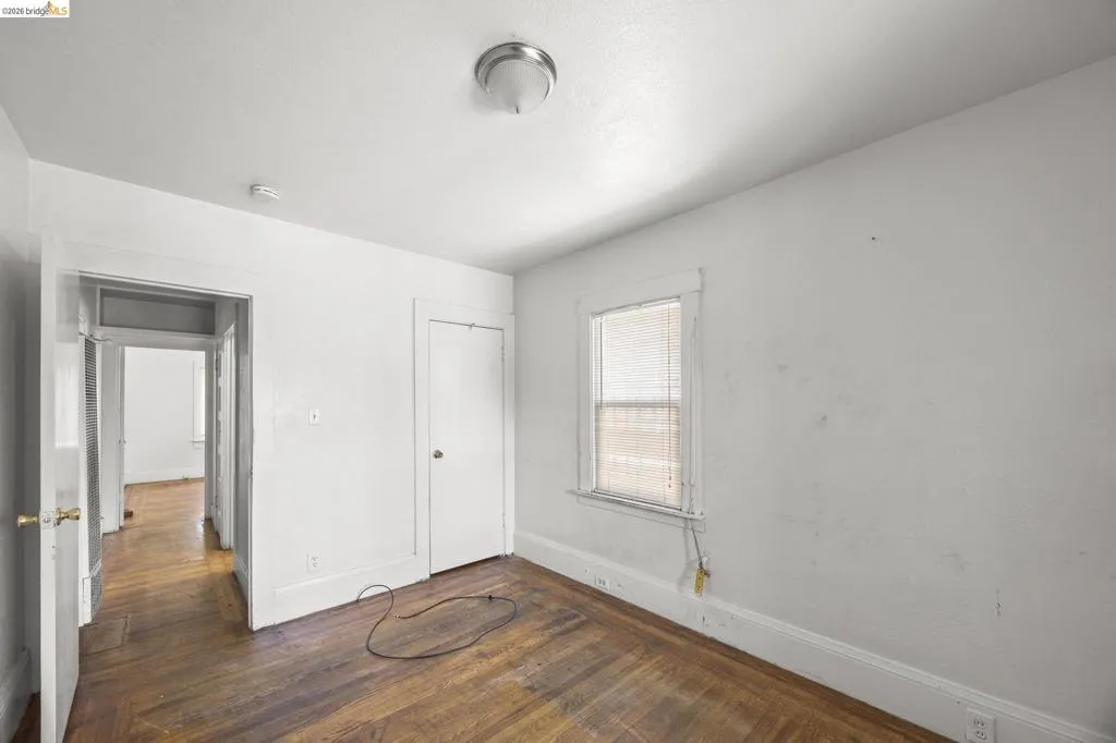 Room featuring wood-finish flooring, a single window with blinds, and white painted walls