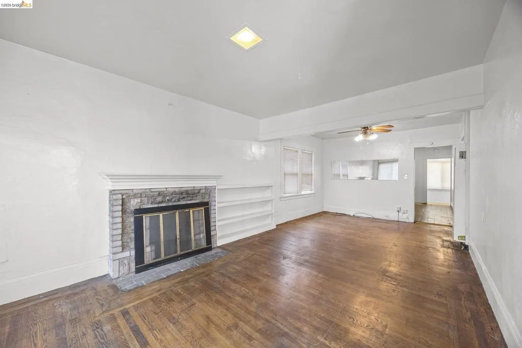 Spacious room featuring wood-finish flooring, a fireplace with a stone surround, and built-in shelving