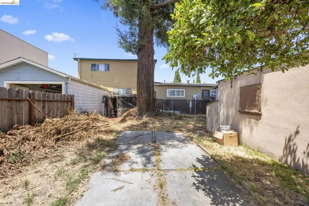 Spacious rear yard featuring concrete paving and a mature tree providing natural shade