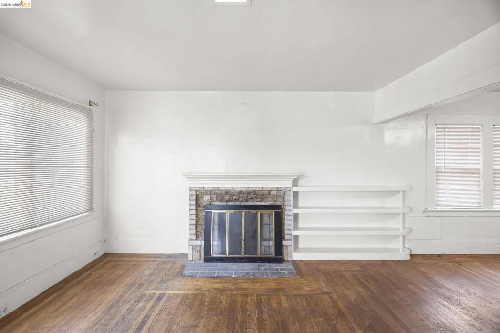 Hardwood flooring throughout featuring a brick fireplace with a white mantel and hearth, built-in shelving, and multiple windows