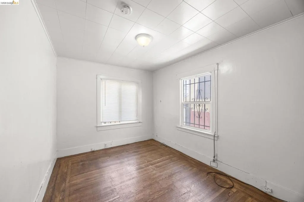 Room featuring wood-finish flooring, two windows providing natural illumination, and a ceiling-mounted light fixture