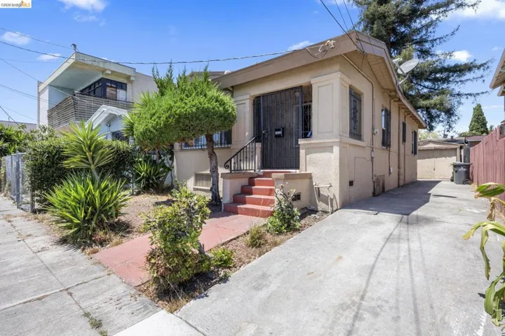 Single-story residence featuring a stucco exterior, concrete driveway, front porch with red-painted steps, and decorative security bars on the front door and windows