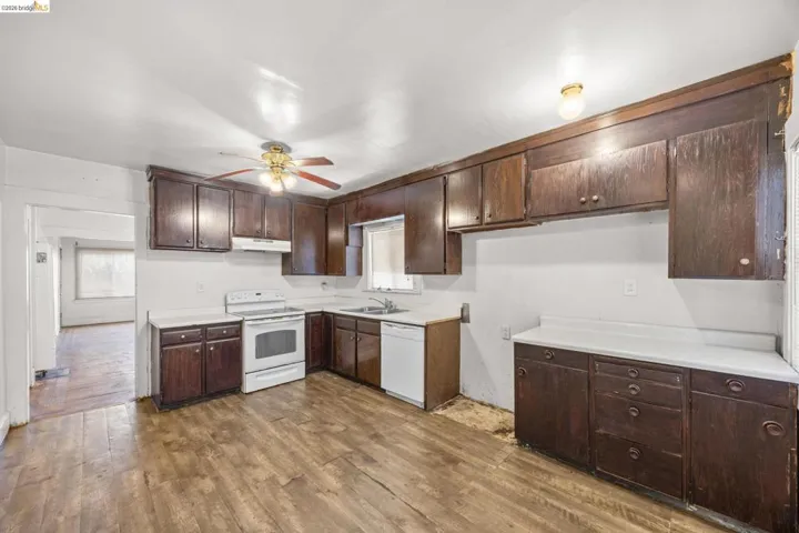 Kitchen featuring extensive dark wood cabinetry, white countertops, white range, white dishwasher, and wood-finish flooring