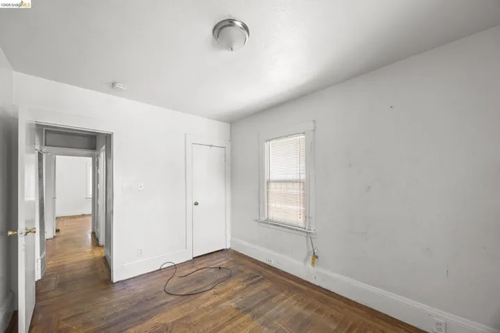 Room featuring wood-finish flooring, a single window with blinds, and white painted walls