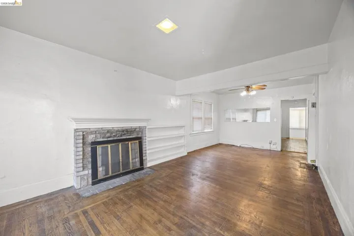 Spacious room featuring wood-finish flooring, a fireplace with a stone surround, and built-in shelving