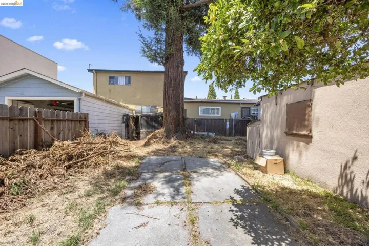Spacious rear yard featuring concrete paving and a mature tree providing natural shade