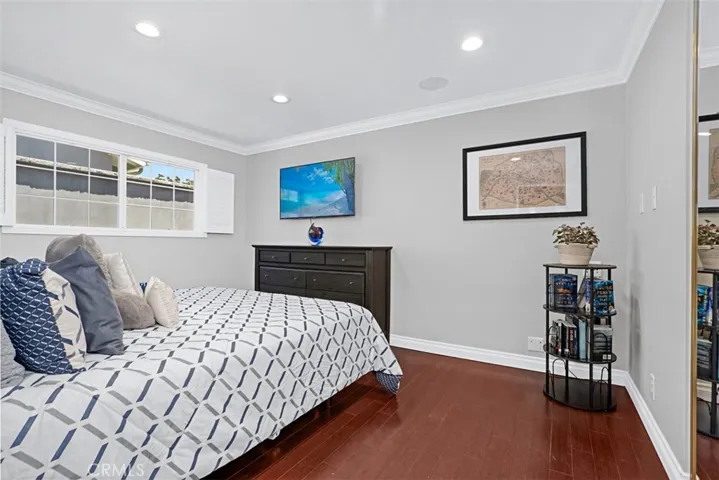Spacious secondary bedroom with rich hardwood flooring, crown molding, recessed lighting, and generous wall space for a variety of furniture arrangements.