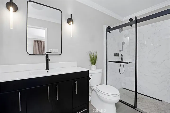 Beautifully remodeled primary bath featuring a custom vanity, designer lighting, matte black fixtures, and a spacious walk-in shower with tile.
