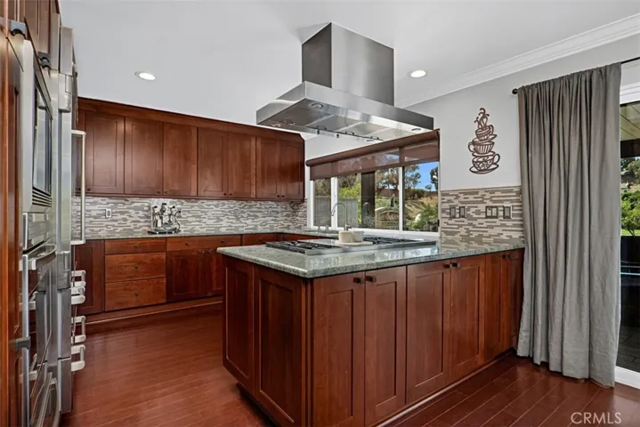 The beautifully remodeled kitchen features custom cabinetry, granite countertops, premium stainless steel appliances, generous workspace, and a center prep island with a Wolf cooktop and designer vent hood.