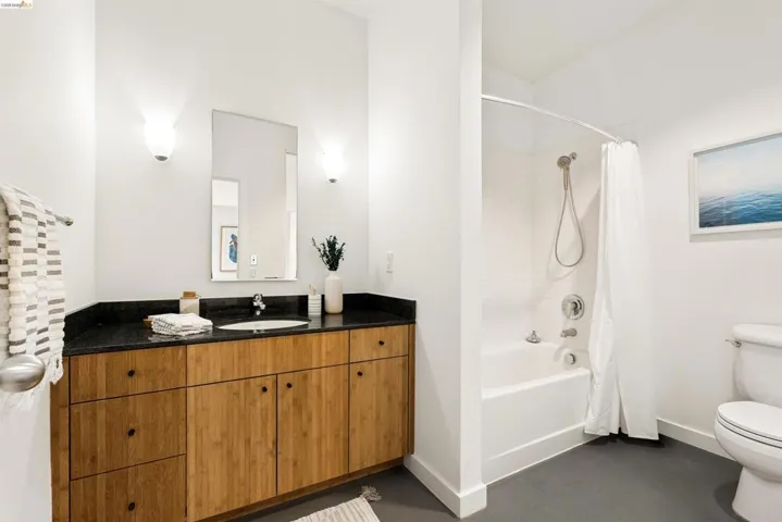Contemporary bathroom featuring a wood-finish vanity with a dark countertop, undermount sink, and wall-mounted sconces