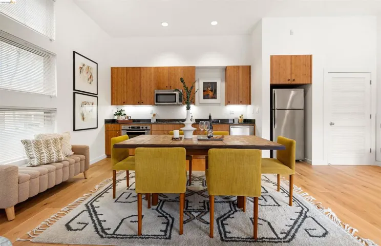 Open-concept kitchen and dining area featuring wood-finish flooring, high ceilings, recessed lighting, stainless steel appliances, and wood cabinetry