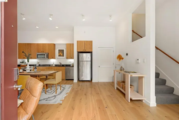 Open-concept living space featuring wood-finish flooring, a kitchen with natural wood cabinetry and stainless steel appliances, and a carpeted staircase with a wood handrail