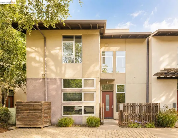 Modern multi-story exterior featuring a red entry door, varied window configurations, and a neutral stucco facade