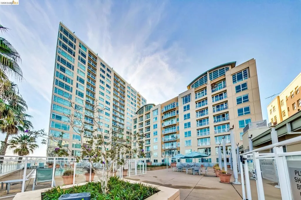 Modern high-rise residential building featuring extensive window-lines, private balconies, and a shared patio area