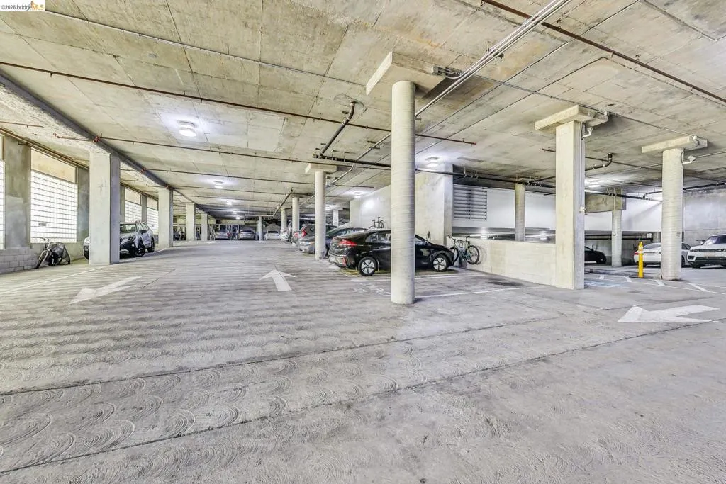 Underground parking garage featuring concrete pillars and ceiling, integrated lighting, painted directional arrows, and multiple vehicle spaces