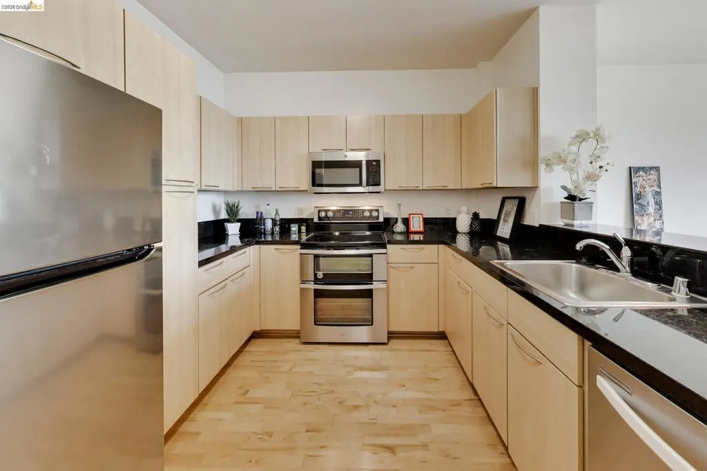 U-shaped kitchen featuring light wood-finish cabinetry, dark stone countertops, and stainless steel appliances