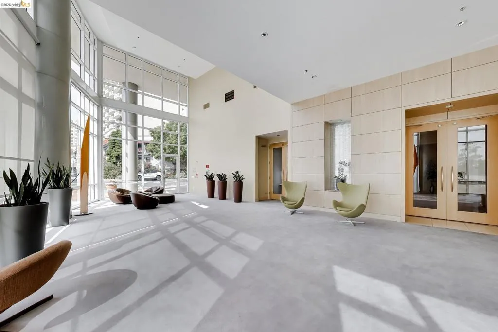 Spacious lobby area featuring extensive window walls, high ceilings, light wood-paneled walls, double glass entry doors, and recessed lighting