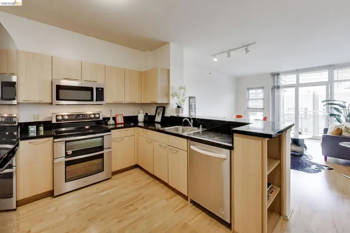 Modern kitchen featuring light wood cabinetry, stainless steel appliances, black countertops, and a built-in breakfast bar