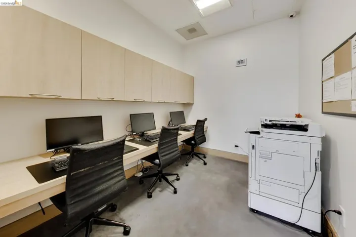 Dedicated workspace featuring a built-in desk, overhead cabinetry with light-toned wood-finish doors, and durable gray flooring