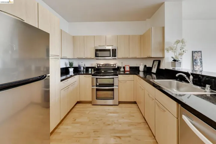 U-shaped kitchen featuring light wood-finish cabinetry, dark stone countertops, and stainless steel appliances