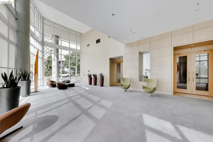 Spacious lobby area featuring extensive window walls, high ceilings, light wood-paneled walls, double glass entry doors, and recessed lighting