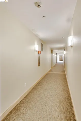 Carpeted hallway featuring wall-mounted sconces, neutral wall tones, and crown molding