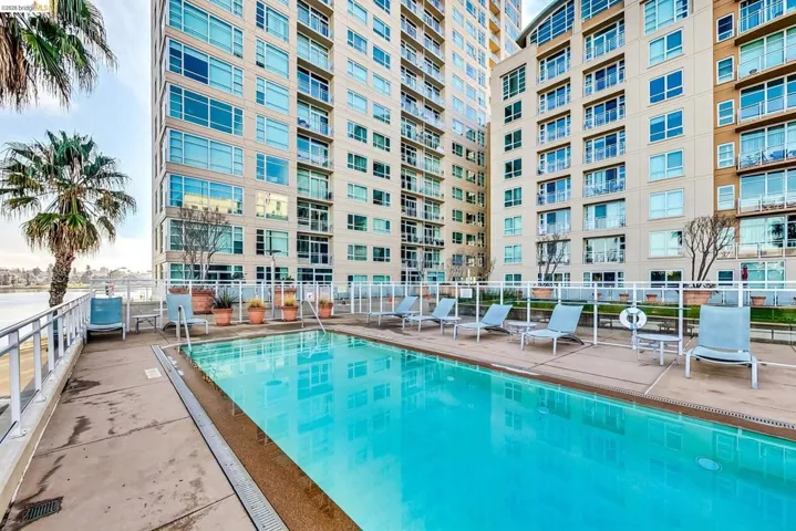 Outdoor swimming pool surrounded by lounge chairs, concrete patio, and a white perimeter fence