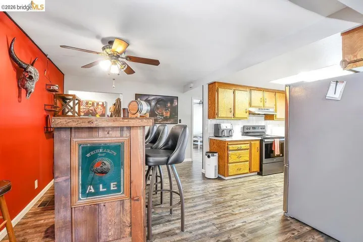 Open concept living space featuring wood-finish flooring, a built-in bar, and a kitchen area with wood cabinetry and a white tile backsplash