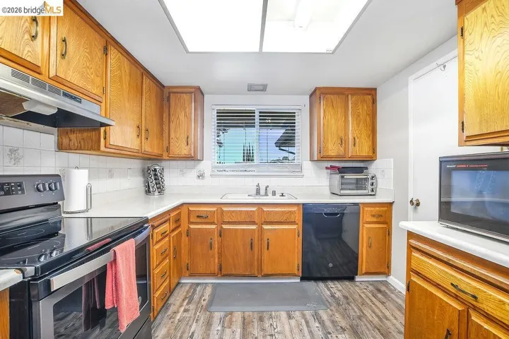 Kitchen featuring wood cabinetry, white countertops, tile backsplash, stainless steel range hood, and wood-finish flooring